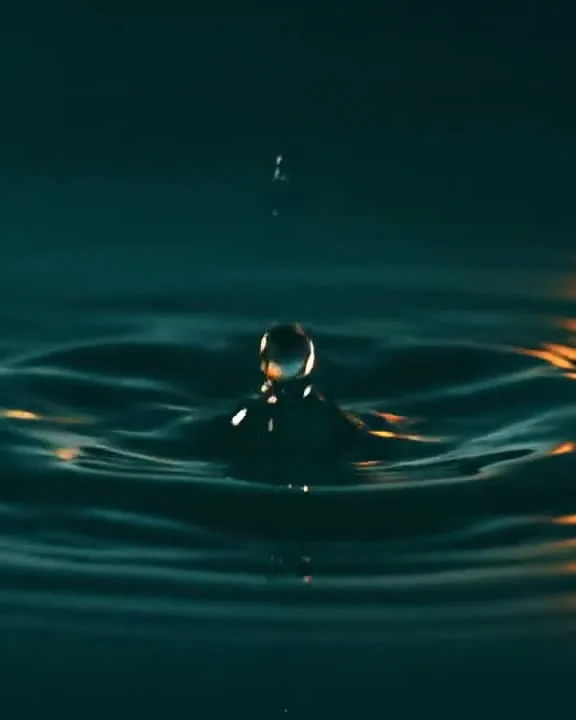 Una goccia rimbalza sulla superficie verde petrolio e solleva una piccola colonna d'acqua